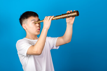 Young Asian boy using spyglass telescope against blue background