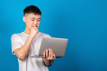 Handsome asian young man teenager in white T-shirt using modern laptop and thinking against blue background