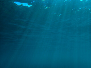 Dark blue ocean surface seen from underwater. Abstract waves underwater and rays of sunlight shining through, Sun light rays undersea deep, Underwater background with sea bottom, Mediterranean sea.