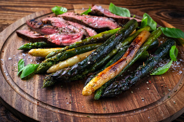Grilled green, white and violet asparagus with roasted dry aged beef steak on rustic wooden board...