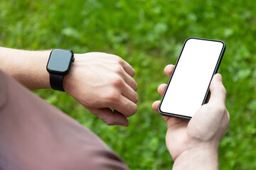 Close up man hands checking his heartbeat with smartwatch and mobile phone at nature park. Male checking pulse after jogging. Fitness tracker. Mock up. Space for design
