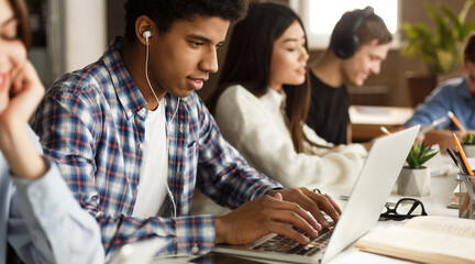 Guy doing project in school library, preparing for lectures on laptop and browse internet, panorama