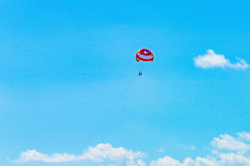 Two people parasailing under a red parachute against a vibrant blue sky in Cancun, enjoying a thrilling aerial adventure High-quality photo