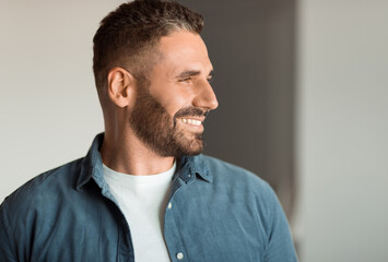Cheerful middle aged man with stubble smiling while looking aside indoor, portrait shot of...