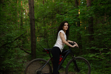 Beauty fun smiling sport woman biking on bicycle on path among green trees in a forest background. Enjoying girl outdoors. Female riding in park in sporty clothes. Closeup portrait