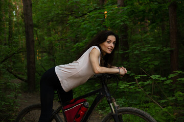 Beauty fun smiling sport woman biking on bicycle on path among green trees in a forest background....