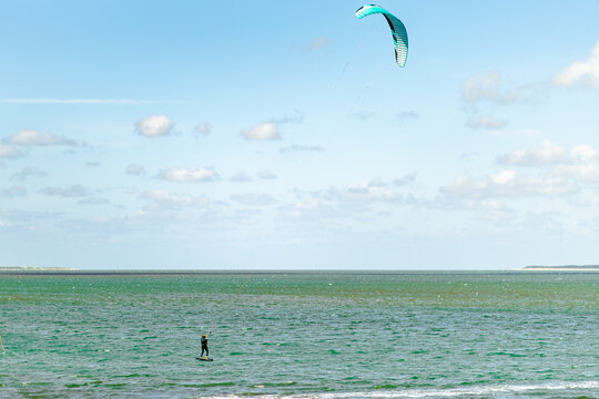 Kite surfer gliding over calm waters at a coastal location on a sunny day with scattered clouds