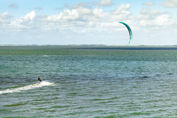 Kite surfer glides over calm waters under a clear sky in a coastal landscape