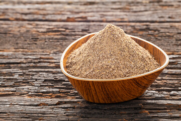 Piper nigrum - Dried and ground organic black pepper in a bowl on a wooden background