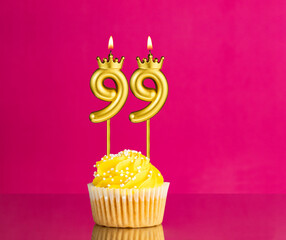 Birthday celebration with number 99 candle - Yellow cupcake on a pink background