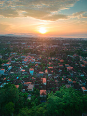 The golden sun rises over the enchanting rooftops and lush greenery of Bali, casting a warm glow.