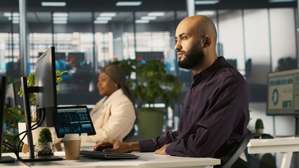 Arab man in office reviewing financial graphs, analyzing key performance indicators. Middle Eastern employee in workspace looking over data trends and strategic insights, camera A