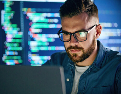 Man focuses intently on his laptop, his brow furrowed in concentration as he navigates complex coding tasks. colorful lines of code in background highlight tech savvy environment