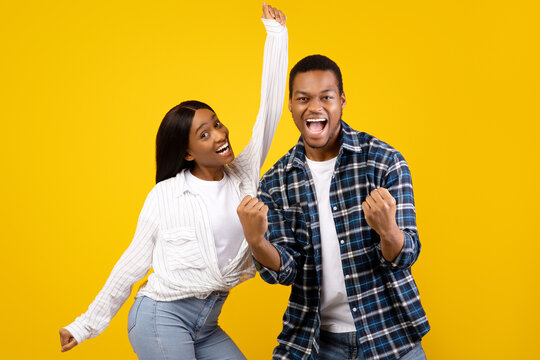 Emotions of victory, celebration and dance. Sincere expression of success young african american male and female with open mouth, screams and rejoices to win isolated on yellow background, studio shot