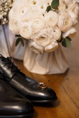 Wedding Day Details Still Life: Black Leather Shoes, Gold Rings, White Ranunculus Bouquet, Dark...