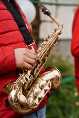 Close-up of a Musician's Hands Holding a Shiny Brass Saxophone with a Red Puffer Jacket Background