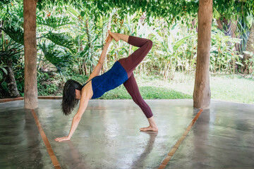 Woman practicing half moon yoga pose in tropical retreat