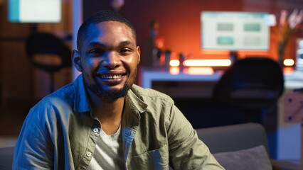 Portrait of black freelancer laying on the sofa and texting on phone, relaxing and smiling in his...