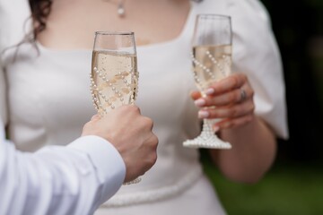 Elegant Wedding Toast: Couple Celebrating with Pearl-Adorned Champagne Flutes in a Lush Outdoor Setting, Romantic Ivory Tones.