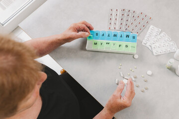 An elderly woman places a pill in a plastic container.