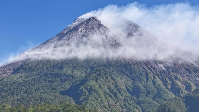  A dramatic and close-up view of Mount Merapi, one of the most active volcanoes in Indonesia. The image captures the rugged peak partially veiled by drifting clouds.