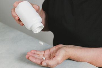 An elderly woman holds capsule pills in her hands.