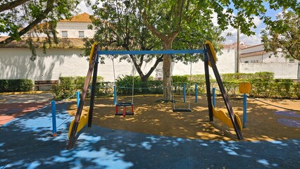 Empty swings in shaded playground surrounded by trees — childhood memories and peaceful atmosphere