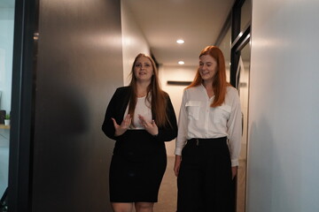 Two women engage in conversation while walking through a modern office corridor