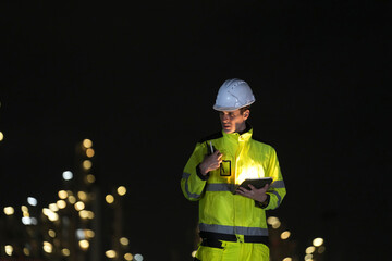 Fototapeta premium Construction worker checking data at night in a brightly lit industrial area
