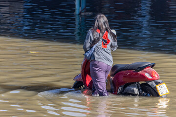 A woman pushes a motorbike through a flooded street, Thailand