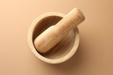 Wooden mortar and pestle on light brown background, top view