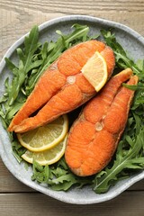 Seafood. Tasty salmon steaks, arugula and lemon on wooden table, top view