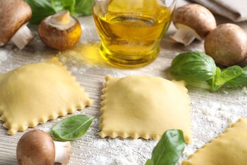 Uncooked ravioli, mushrooms and basil on white wooden table, closeup