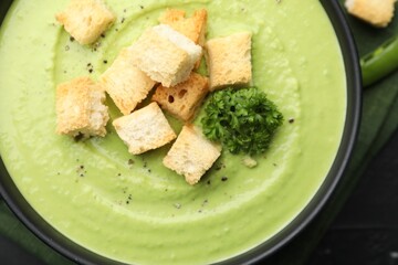 Tasty pea cream soup with croutons and broccoli on black table, top view