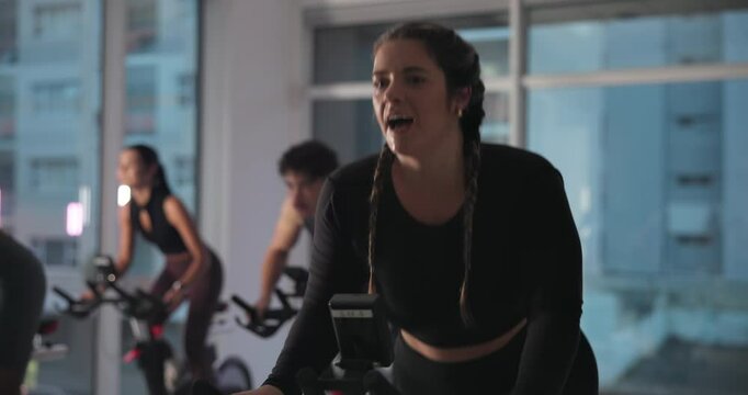 Woman, bike and spin class at gym with smile, strobe lights and coach with motivation for fitness. Person, happy and talk with cycling, workout and training for challenge with group at exercise club