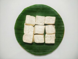 Top-Down Shot of a Group of Plain Tofu Pieces Artfully Arranged on a Banana Leaf Platter, Creating...