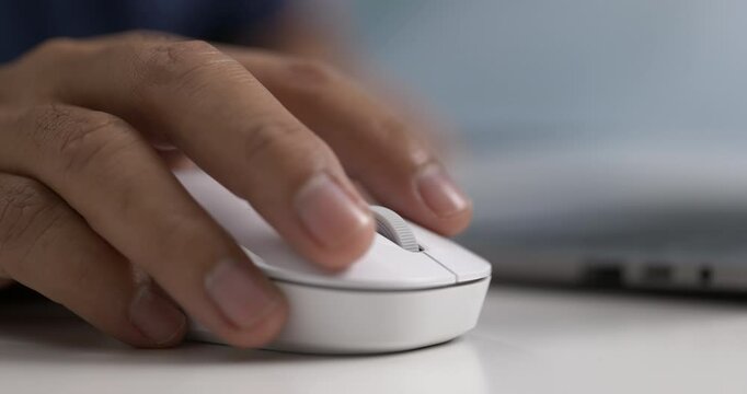 Close-up of hand using white wireless mouse near laptop on modern white desk.