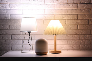 Different glowing lamps on table near white brick wall in dark room