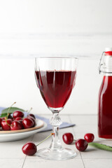 Glass of sweet cherry liqueur with berries on white tile table