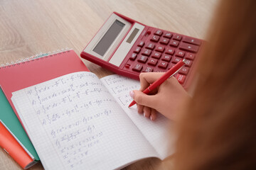 Woman writing math formulas in copybook on wooden table
