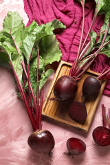 Wooden board of fresh beets with green leaves on pink background