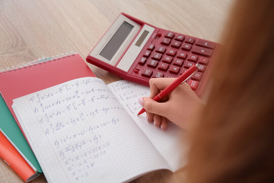 Woman writing math formulas in copybook on wooden table