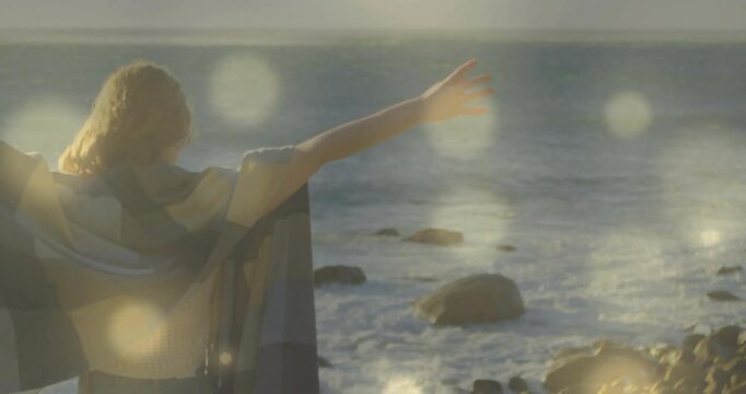 Woman lifting arms on rocky shore unfolding shawl with crashing waves for travel marketing