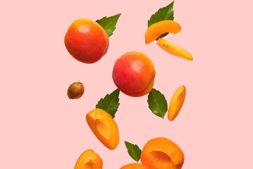 Flying fresh apricots with pieces and leaves on pink background