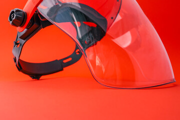 Protective face shield with transparent visor and orange headgear, isolated on bright red...