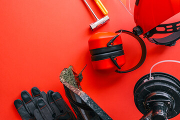 Complete brush cutter equipment set including trimmer head, safety helmet with face shield, ear protectors, gloves, screwdriver, socket wrench and nut, arranged on red background