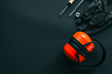 Flat lay of brush cutter head, protective helmet with face shield, ear muffs, gloves, screwdriver, wrench and nut on black background, complete gardening and landscaping safety set