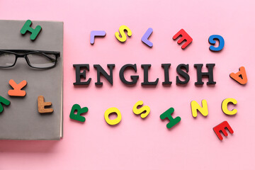 Word ENGLISH with eyeglasses, notebook and wooden letters on pink background
