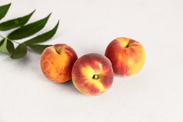 Sweet peaches and leaves on white table