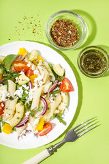Plate of tasty pasta salad with tomatoes and avocado on green background